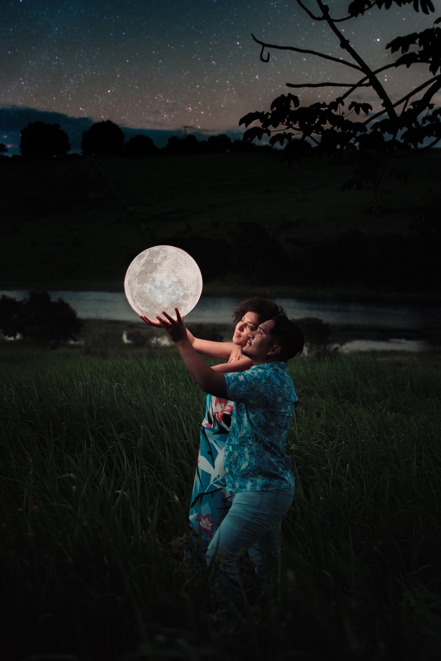 man and woman holding up a moon like illuminated spherical ball outdoor at night