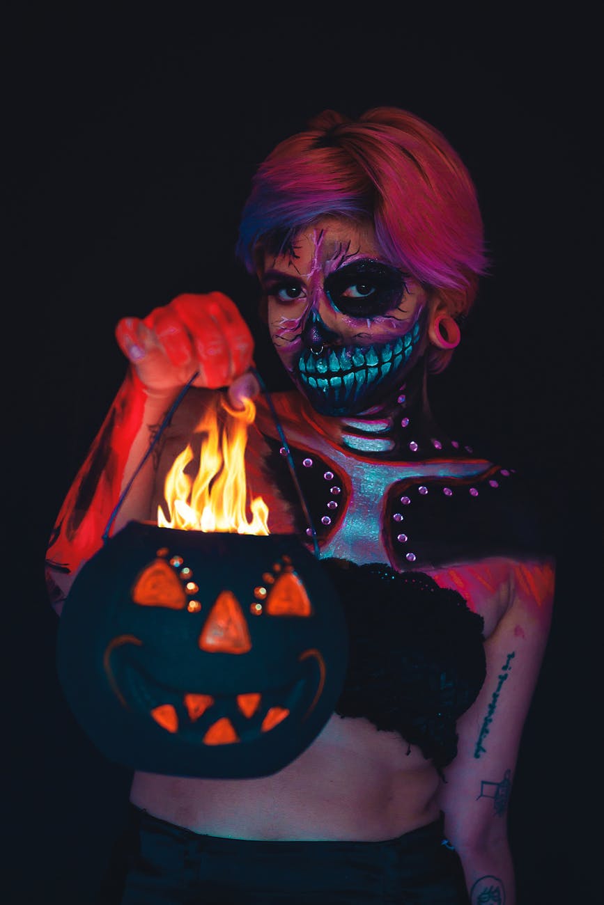 woman with a face and body painting holding a halloween pumpkin bucket