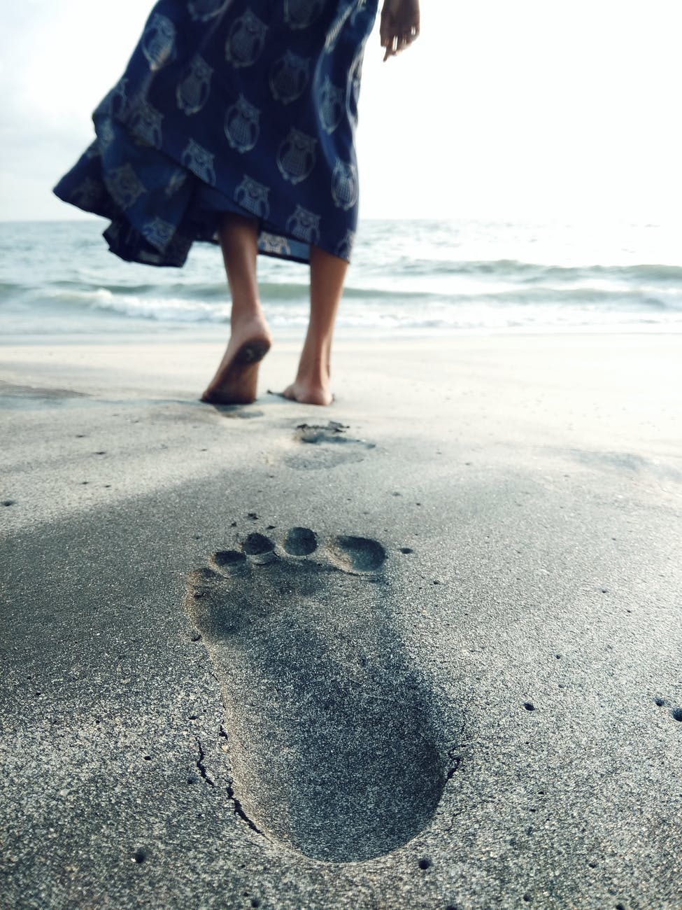 photo of woman walking barefoot on seashore
